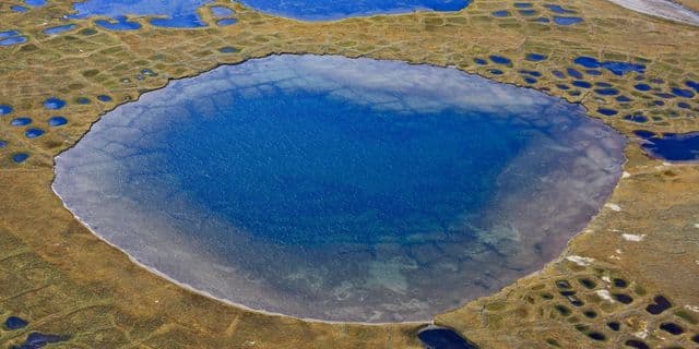 Paisagem de tundra com solo degelado e vegetação sob céu nublado